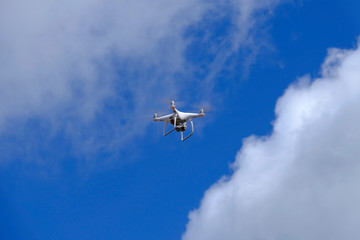 White drone quadcopter flying on the air for take a photo and video with white cloudy and blue sky background.