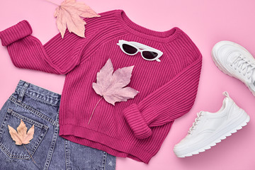 Fall fashion Flat lay. Trendy pink jumper, Stylish hipster sneakers, sunglasses, denim, autumn Maple Leaf. Creative Woman Clothes Accessories layout.Fall Girl fashionable Outfit, autumnal pastel color