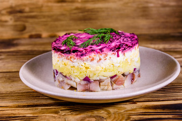 Ceramic plate with russian traditional new year salad herring under fur coat (shuba) and on rustic wooden table