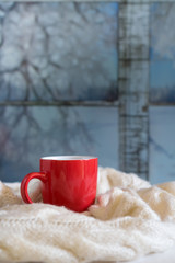 Obraz na płótnie Canvas Cozy winter still life: mug of hot tea and warm woolen knitting on vintage windowsill against snow landscape from outside.