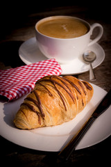 Coffee cup and fresh baked croissants on wooden background.