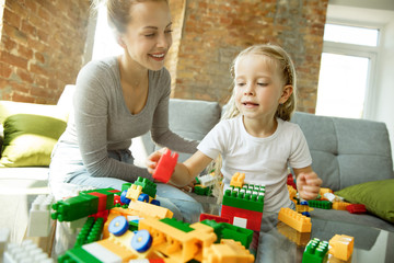 Female caucasian teacher and little girl, or mom and daughter. Homeschooling. Sitting on the sofa with plastic constructor, learning, talking and having fun. Education, school, studying concept.
