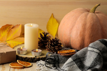 Candles, cones and decorative pumpkins and autumn yellow leaves on a natural wooden table. autumn composition. comfort. decor