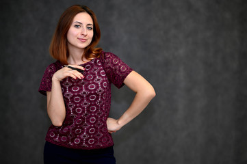 Portrait of a brunette girl with beautiful brown hair in a purple t-shirt on a gray background. He stands in different poses, demonstrates emotions.