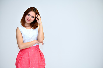 Portrait of a brunette girl with beautiful brown hair in a pink and white dress on a white background. He stands in different poses, demonstrates emotions.