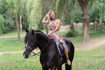 Obraz premium Young woman in a bright colorful dress riding a black horse