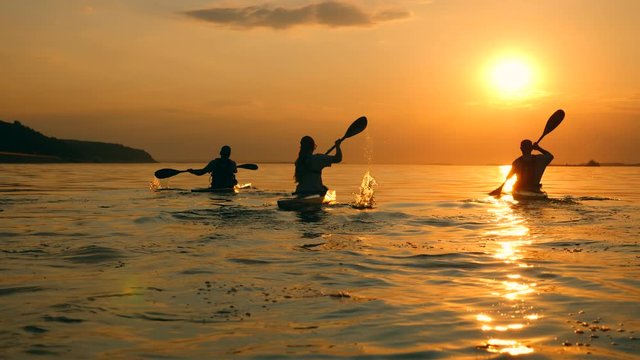 The sun is setting and people are sailing in canoes