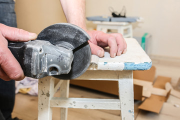 Man is cutting baseboard. Repair works indoors. Renovation in the flat.  Angle grinder in hands.