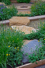 Modern water garden with flowing rill with rocks, stepping stones and rockery feature with flowers and plants