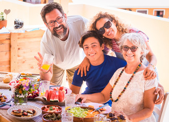 Happy and smiling multi-generation family. Beautiful couple with teenager's son and grandmother enjoying brunch or meal together. Sunlight on the terrace field. Family and love concept