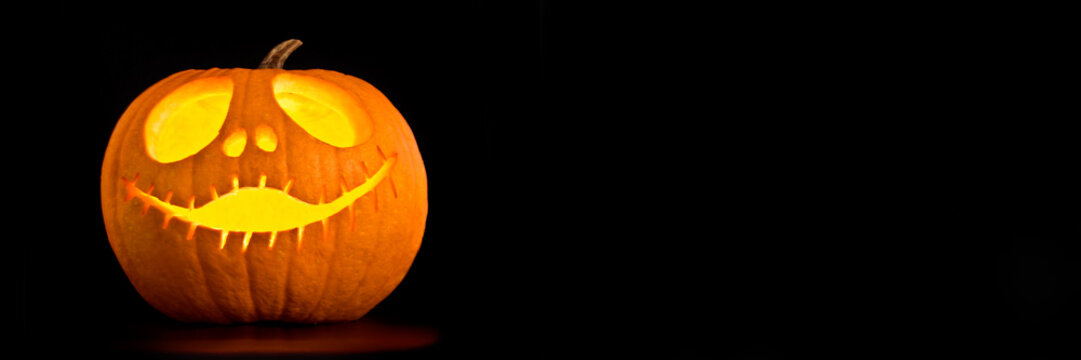 Illuminated Halloween Jack-o-lantern pumpkin, black panoramic background with copy space