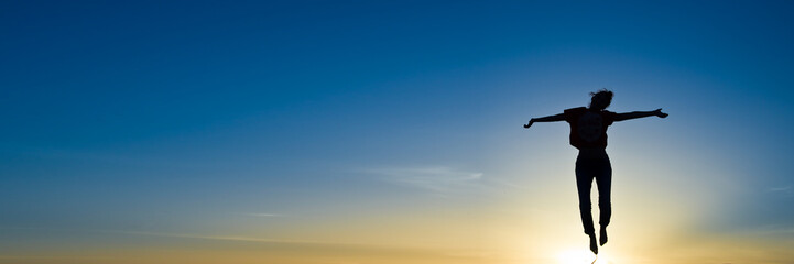 Silhouette of a woman jumping in the sunset, panoramic sky background with copy space