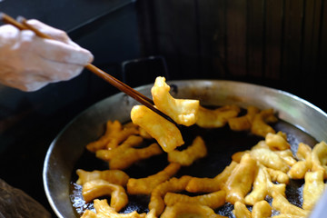 A shop owner tongs up a snack from a hot pan