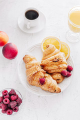 Breakfast with croissants, a cup of coffee, raspberries, peaches and orange juice, top view