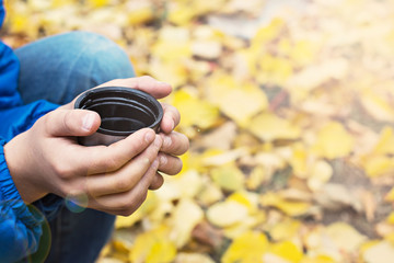 hot drink, cocoa, tea in a mug from a thermos in children's hands on a background of yellow autumn leaves.