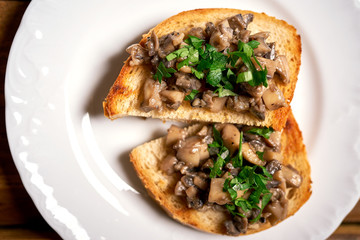 Toasts with mushrooms on white plate on wooden kitchen table