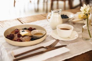 Photo closeup of breakfast meal and cutlery. Pancakes with berries, milk, coffee on kitchen table