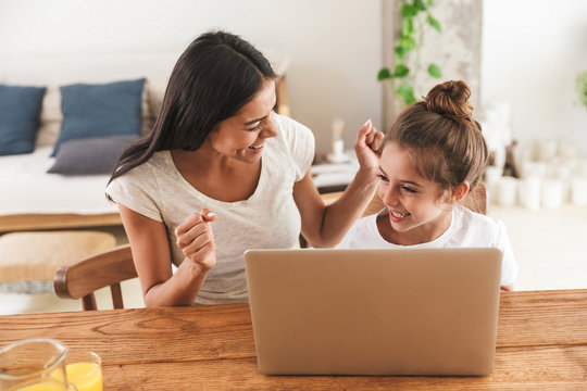 Image of cheerful family woman and her little daughter smiling and using laptop computer together in apartment
