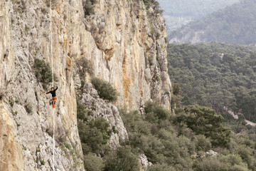 A man is walking along a stretched sling. Highline in the mountains. Man catches balance. Performance of a tightrope walker in nature. Highliner on the background of valley.