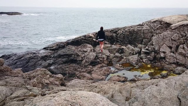 woman climbs rocky sea shore