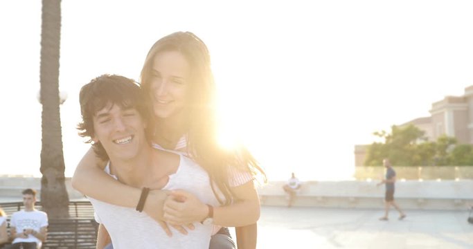 Two beautiful teenager friends or young couple having fun together, giving her piggyback rides, in the city in spring or summer. Young boy and girls amuse themselves in the town.
