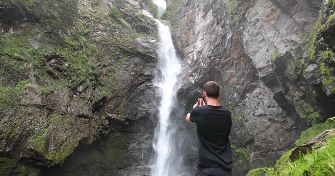 Traveler shooting a waterfall in the Swiss alps with his cellphone.
