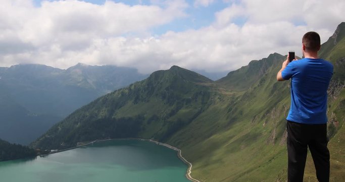 Young man taking a video of Lake Ritom in Switzerland with his mobile phone.