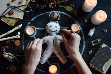 In Voodoo doll are needles pricked. Candles, pentagram, stones, love potion and old books on witch table. Occult, esoteric or divination concept. Mystic, Halloween and vintage background