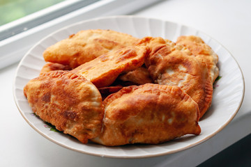 Chebureks. Appetizing homemade pasties in a plate on the windowsill.