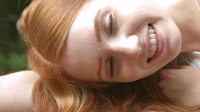 Close up of redhead woman lying down and smiling at camera. Static. Slowmo