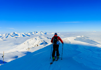 Fototapeta na wymiar Ski in winter season, mountains and ski touring man on the top in sunny day in France, Alps above the clouds.