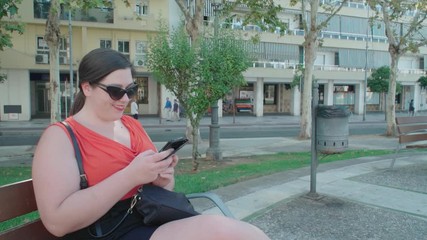 Young woman texting and smiling on bench in downtown park - Powered by Adobe
