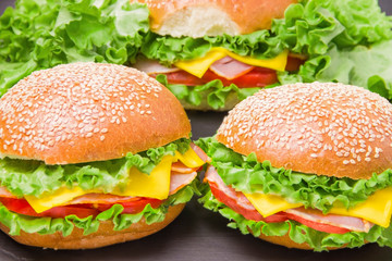 Three sandwiches with ham, tomato, cheese and lettuce on a black background. Nearby are leafs of lettuce.