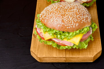sandwich with ham, cheese, lettuce and tomato on a wooden board. Food on a black background. fast food.