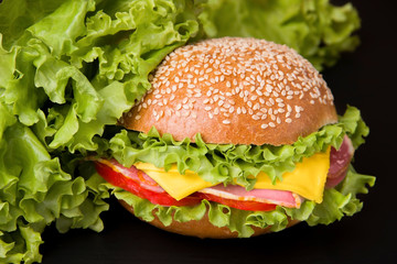 Sandwich with ham, tomato, cheese and lettuce on a black background. Nearby are leafs of lettuce.