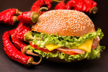 Bun with ham, cheese, herbs and tomato. Red pepper next to the board. Sandwich. Dinner. Fast food