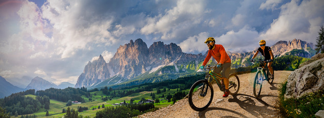 Couple cycling on electric bike, rides mountain trail. Woman and Man riding on bikes in Dolomites mountains landscape. Cycling e-mtb enduro trail track. Outdoor sport activity. - 289060139