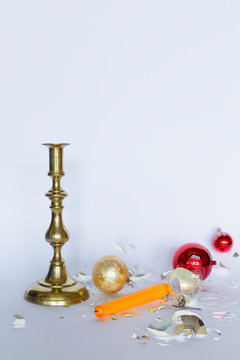 Front view of falling and shattered red and silver Christmas baubles and a bronze candleholder with a yellow candle on white background