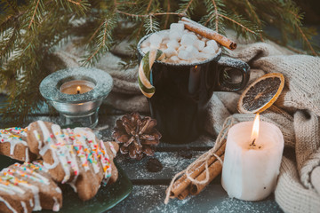 1 mug with hot chocolate and marshmallows, cinnamon stick and Lollipop, candle, spruce branch on a dark background, cone, cookies, knitted fabric