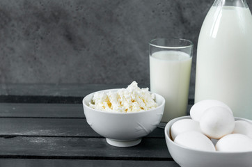  plate of natural cottage cheese, a few white eggs, a glass of cow's milk, a bottle of milk on a gray background