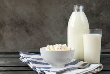 glass of cow's milk, a plate of natural cottage cheese on a towel on a gray background,