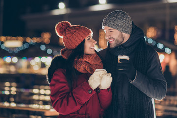 Photo of two people with hot tea beverage in hands celebrating x-mas eve in magic outdoors atmosphere wearing warm jackets