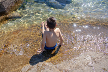 young boy sat on a rock on the beach