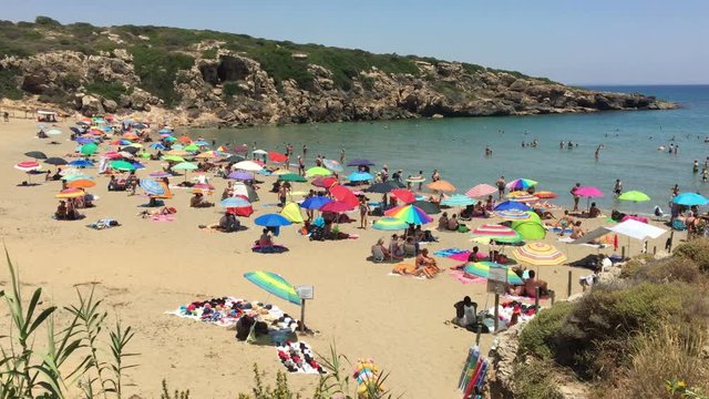 Bathers and umbrellas on the sandy beach of Cala Mosche in Sicily, Italy.