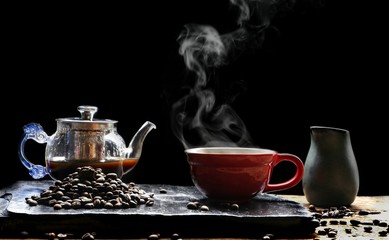 Hot coffee in red coffee cup with steam,  glass coffee pot, milk jug and roast coffee beans on black stone plate with wooden table floor in dark vintage tone style,  selective focus