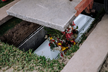 Cement slab was lowered to cover the coffin. Casket of the dead, with flowers from family and...