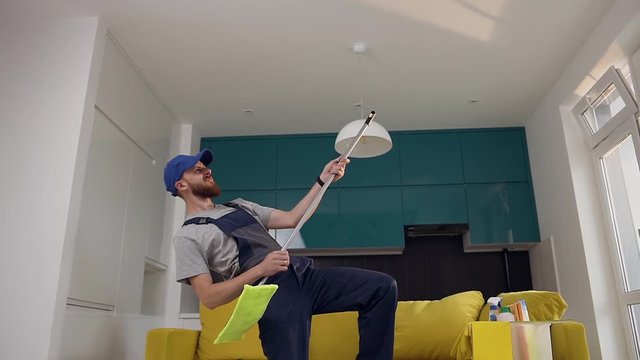 Amusing bearded man from cleaning service playing rock music using a mop as a guitar