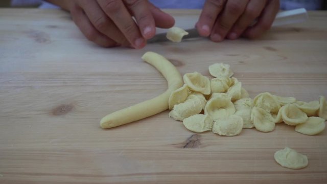 Slow motion video of hands of woman making orecchiette pugliesi pasta  from dough process. Typical italian food from Apulia, Puglia