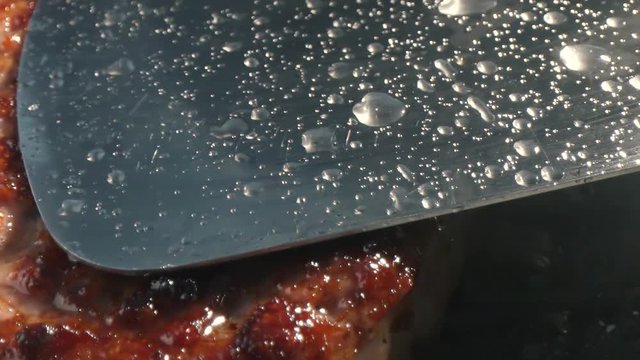 Close-up big beef cutlet is grilled, the chef presses the cutlet with an iron spatula to the grill. Slow motion video