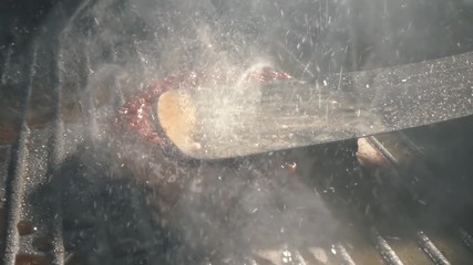 Close-up big beef cutlet is grilled, the chef presses the cutlet with an iron spatula to the grill. Slow motion video